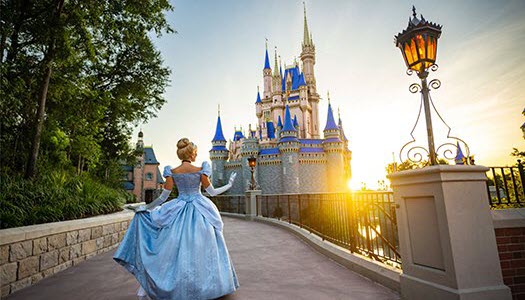 Cinderella in a blue gown walking towards Cinderella Castle at Walt Disney World Resort during sunset.