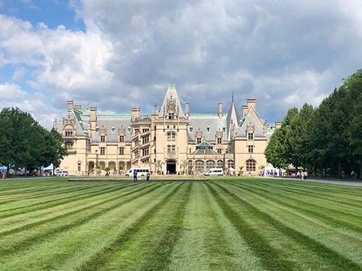 Biltmore Estate mansion with manicured lawn and trees, showcasing a historic travel destination for leisure and corporate trips.