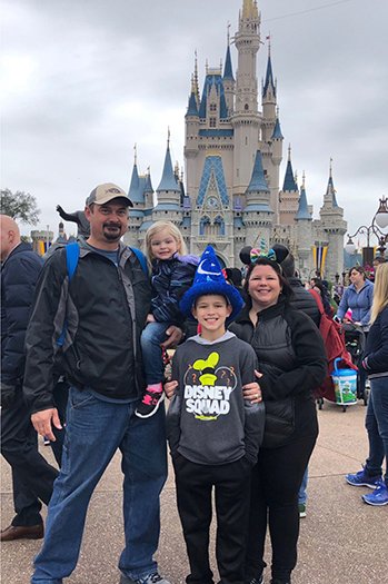 image Family posing in front of Cinderella Castle at Disney World, with children wearing themed hats and shirts, capturing a joyful moment during their magical vacation.